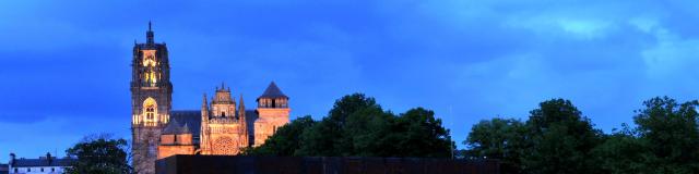 Vue de nuit du musée Soulages entouré d'arbres et de la cathédrale de Rodez en fond