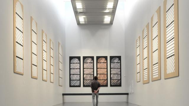 Personne au centre de la Salle de préparation aux vitraux de Conques avec des cartons aux murs et des photos du rendu final selon la luminosité