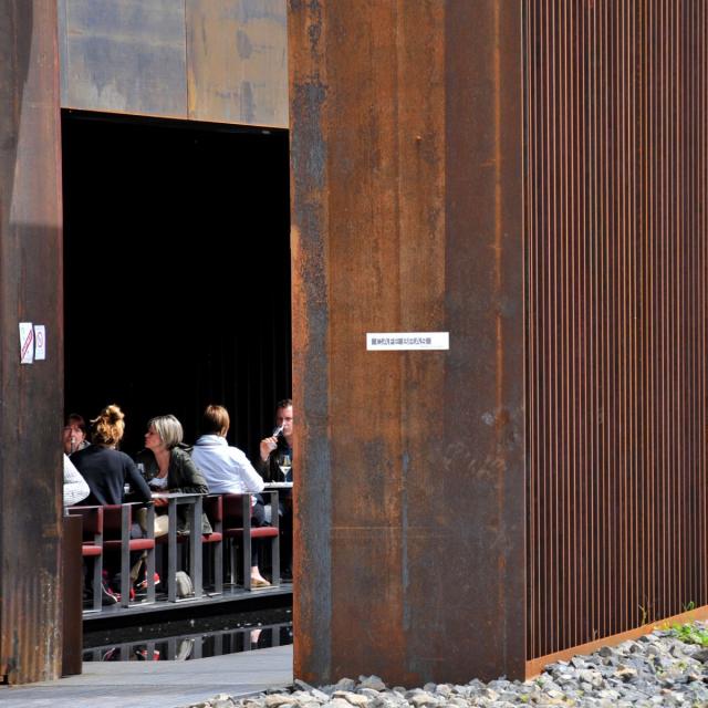 Personnes en train de déjeuner en terrasse au Café Bras, vues depuis l'entrée du restaurant