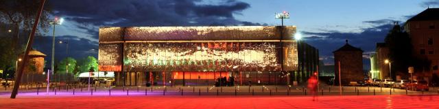 Salle des fêtes de Rodez brillante et son esplanade vues de nuit avec un éclairage rouge contrastant avec la nuit bleue