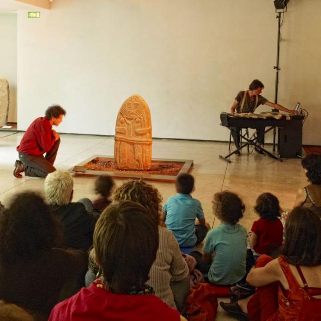 Nombreuses personnes autour d'une statue-menhir, lors d'un atelier au Musée Fenaille de Rodez