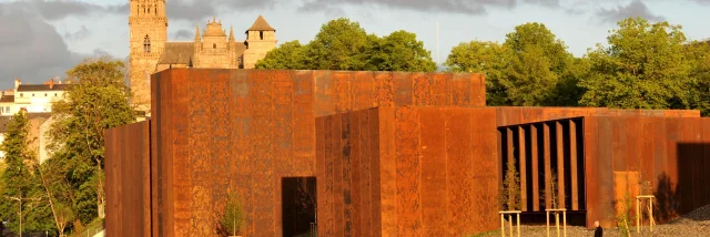 Vue du musée Soulages en acier Corten, passants en dessous et cathédrale en arrière-plan