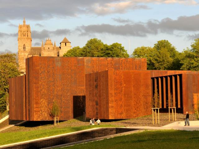 Vue du musée Soulages en acier Corten, passants en dessous et cathédrale en arrière-plan