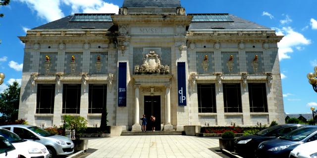 Façade principale du musée des Beaux-Arts Denys-Puech à Rodez, avec ses chiens jaunes sculptés et médaillons, devant un parking