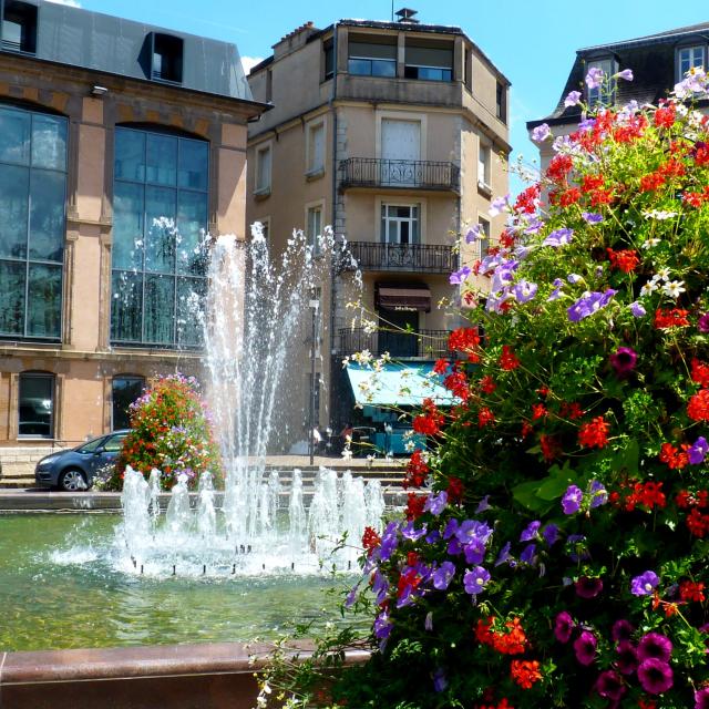 Place de la mairie à Rodez avec sa fontaine et ses compositions florales, au milieu de bâtiments imposants