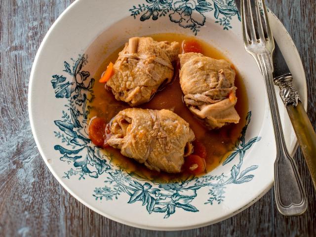 Assiettes de trois tripous dans leur sauce avec des carottes, sur une table en bois avec une fourchette et un couteau