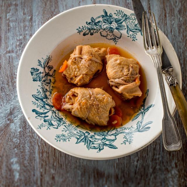 Assiettes de trois tripous dans leur sauce avec des carottes, sur une table en bois avec une fourchette et un couteau