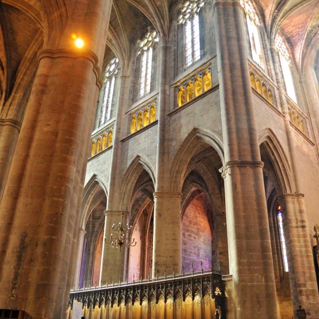 Groupe de personnes tournées vers les stalles en bois, sous les arches du plafond en pierre, sous les ouvertures vitrées et le triforium à l'intérieur de la cathédrale gothique