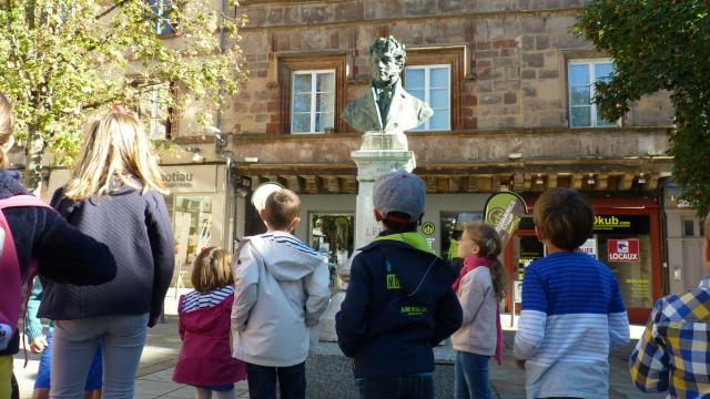 Groupe d'enfants en visite guidée, devant une sculpture sur la place du Bourg