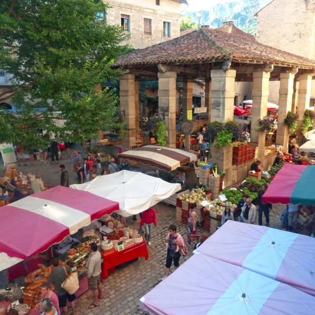 Foule de personnes au marché de Saint Antonin Nobleval avec ses étals et ses parasols, à l'intérieur et à côté des halles ouvertes