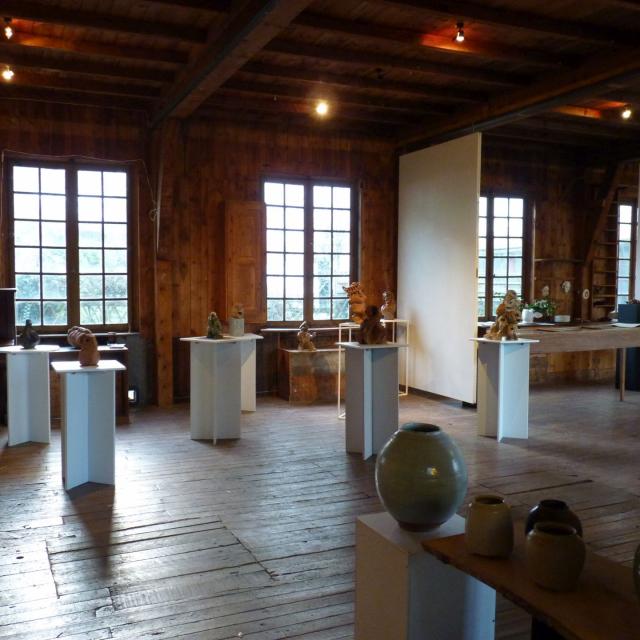 Exposition de sculptures en terre sur des tables hautes carrés blanches, dans la salle lambrissée de La Menuiserie