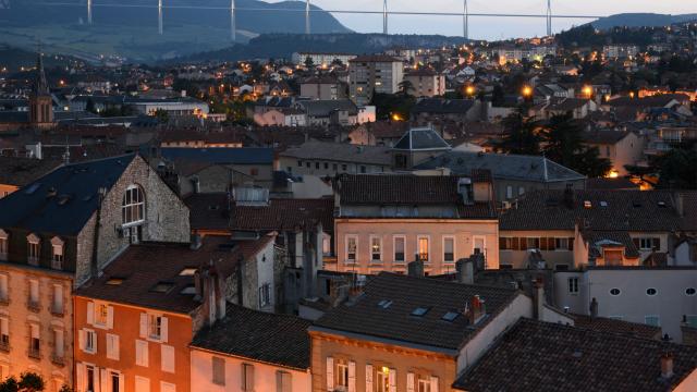 Vue sur la ville de Millau illuminée à la tombée de la nuit et son Viaduc au loin