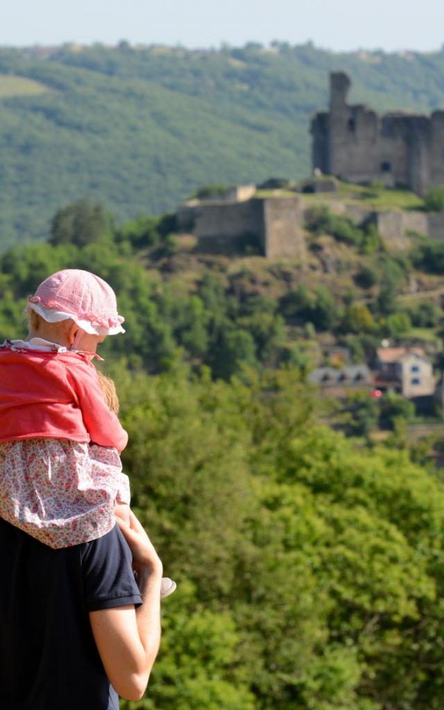 Un homme avec une petite fille sur ses épaules face à la vue sur la forteresse de Najac et la nature environnante