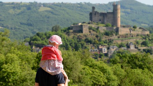 Un homme avec une petite fille sur ses épaules face à la vue sur la forteresse de Najac et la nature environnante