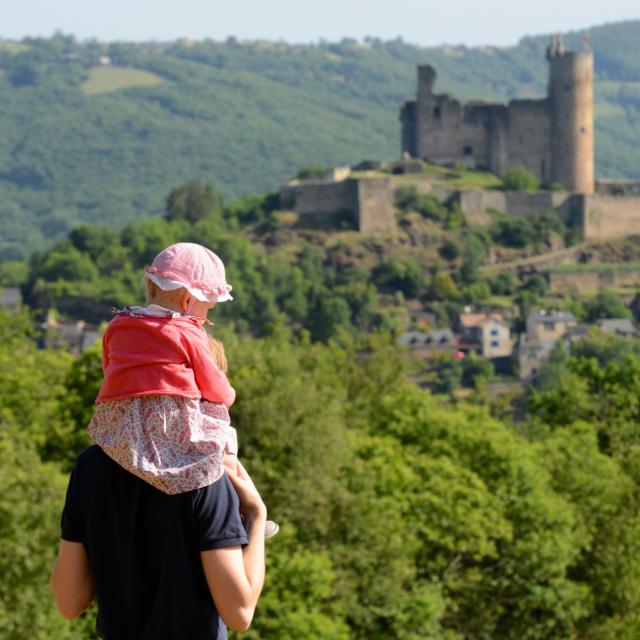 Un homme avec une petite fille sur ses épaules face à la vue sur la forteresse de Najac et la nature environnante