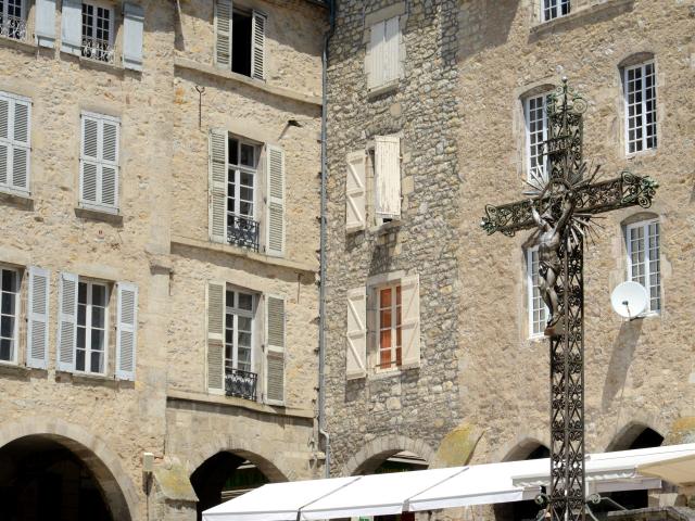 Croix avec le Christ en fer, au bord d'une place où un enfant joue avec une fontaine