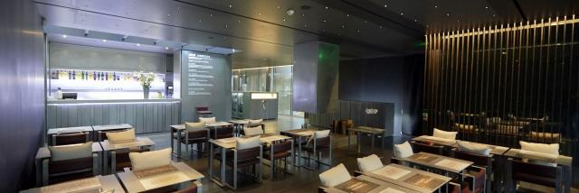 Salle de restaurant du Café Bras avec des fauteuils dotés de coussins blancs, des tables avec des sets, dans un environnement feutré