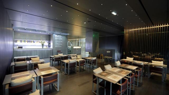 Salle de restaurant du Café Bras avec des fauteuils dotés de coussins blancs, des tables avec des sets, dans un environnement feutré