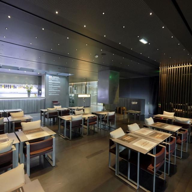 Salle de restaurant du Café Bras avec des fauteuils dotés de coussins blancs, des tables avec des sets, dans un environnement feutré