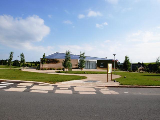 Bâtiment de la mairie de Druelle-Balsac, au bord d'un parc arboré et derrière un panneau signalétique de randonnée