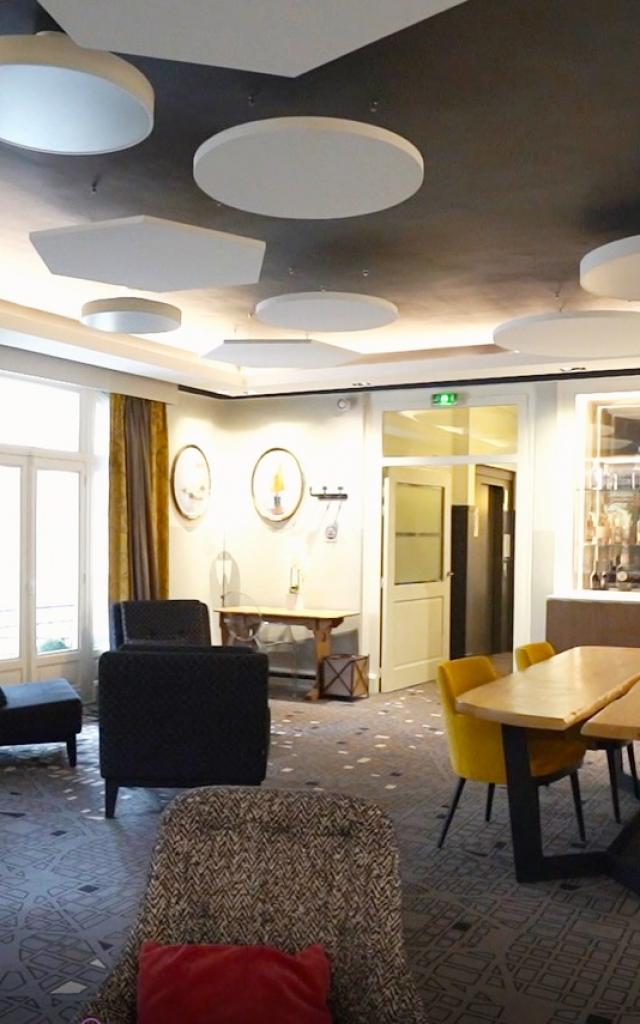 Salon de l'Hôtel Mercure de Rodez avec ses fauteuils confortables, sa table en bois, ses rideaux jaune et gris, ses luminaires ronds modernes