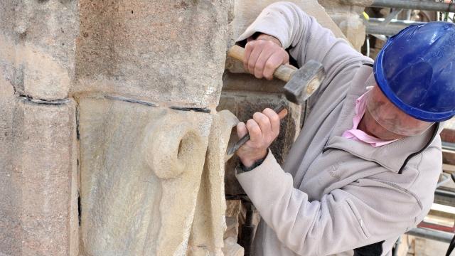 Ouvrier casqué qui taille la pierre de la cathédrale à l'aide d'un marteau et d'un burin