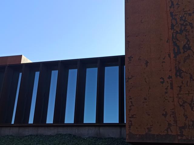 Jeu de matières et de contrastes : le verre des fenêtres avec un reflet bleu du ciel et les murs en acier Corten aux teintes de couleur rouille, au musée Soulages