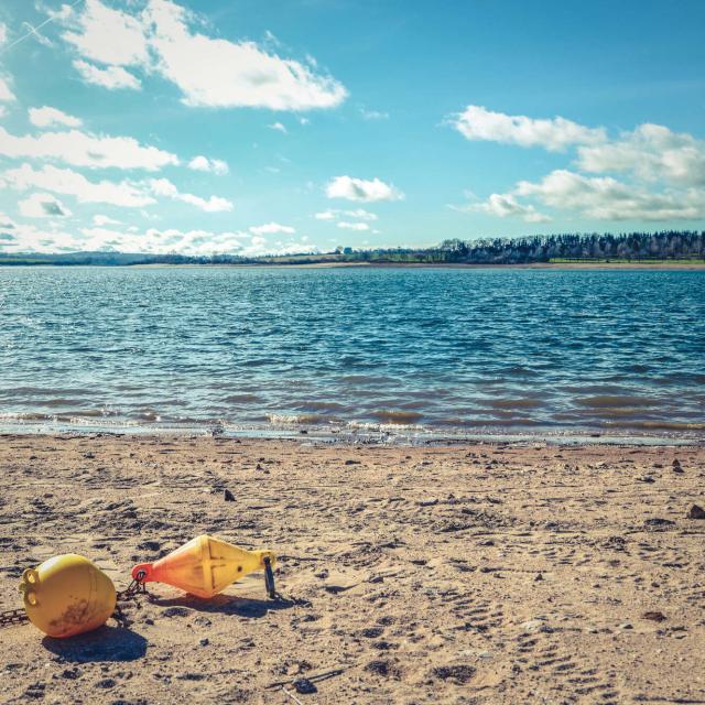 Plage au bord du lac de Pareloup, avec une bouée d'amarrage jaune sur le sable