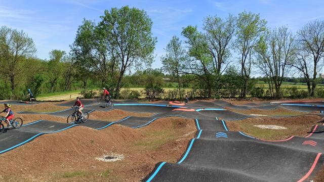 Enfants à vélo ou à trotinette sur les pistes gourdonnées et vallonnées bleu ou rouge d'un pumptrack