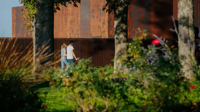 Couple se promenant dans le jardin à côté du musée Soulages au bardage en acier Corten couleur rouille