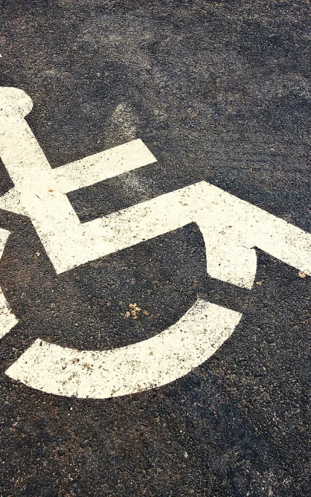 Peint en blanc, sigle au sol sur une place de parking goudronné, signifiant un emplacement pour personne à mobilité réduite