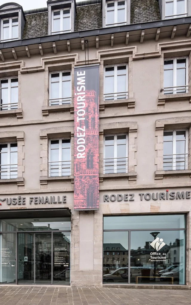 Devanture vitrée de l'office de tourisme et du musée Fenaille, avec des bandeaux verticaux découlant du bâtiment