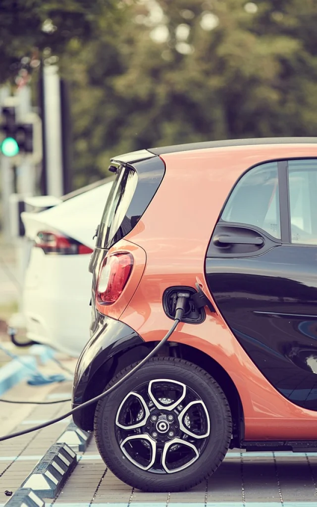 Voitures électriques reliées à une borne de recharge par un câble, sur un parking extérieur dédié