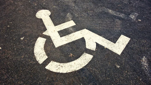 Peint en blanc, sigle au sol sur une place de parking goudronné, signifiant un emplacement pour personne à mobilité réduite